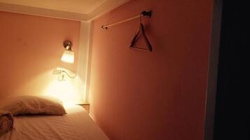 A bedroom with a bed, a hanging light, and a clothes hanger on the wall.