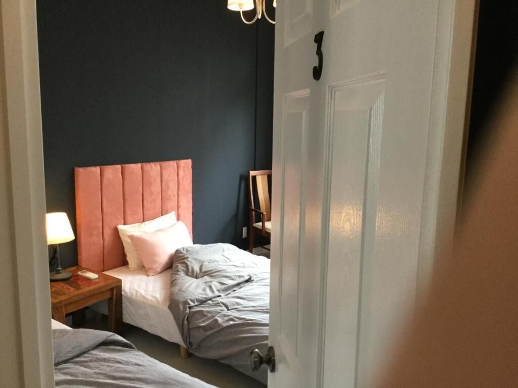 Une chambre d’hôtel avec deux lits, une table de chevet en bois avec une lampe et une porte dotée d’une poignée.