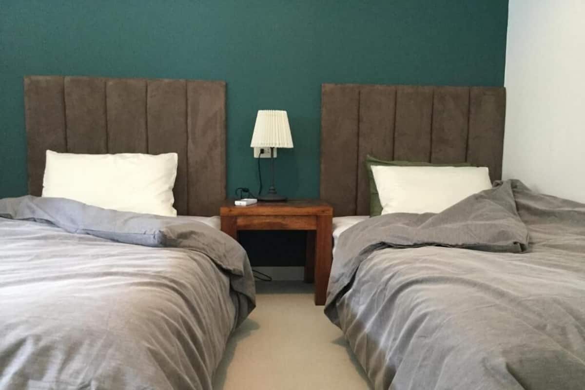 A room with two beds, a nightstand with a lamp, and a teal-colored wall.