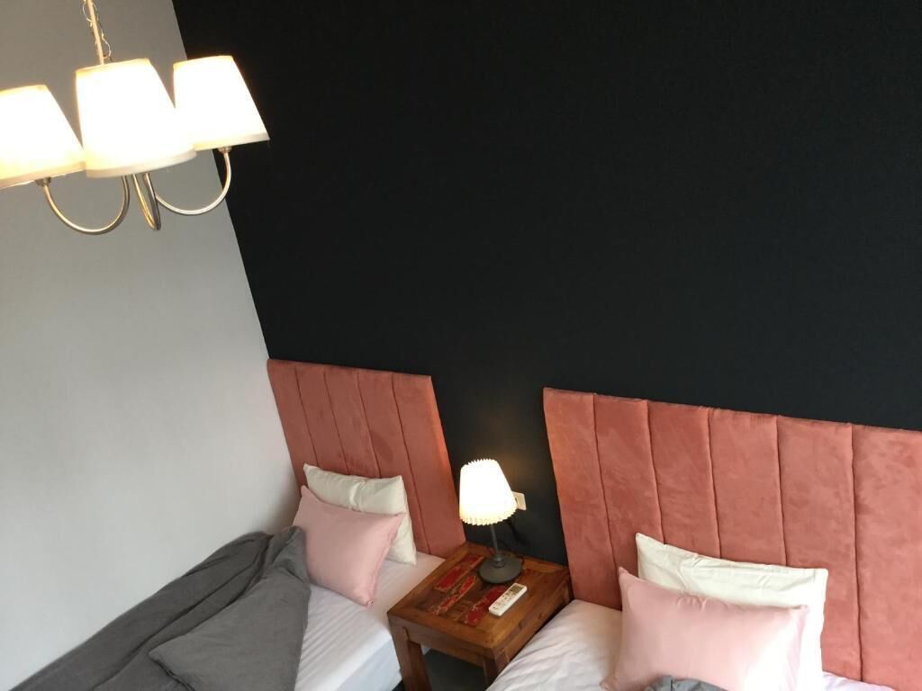A hotel room with two beds, a nightstand with a lamp, and a modern chandelier.