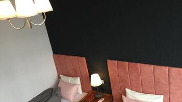 A hotel room with two beds, a nightstand with a lamp, and a modern chandelier.