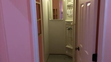 Un área de ducha pequeña y cerrada con puerta de vidrio, un espejo sobre el lavabo y un estante con artículos de aseo.