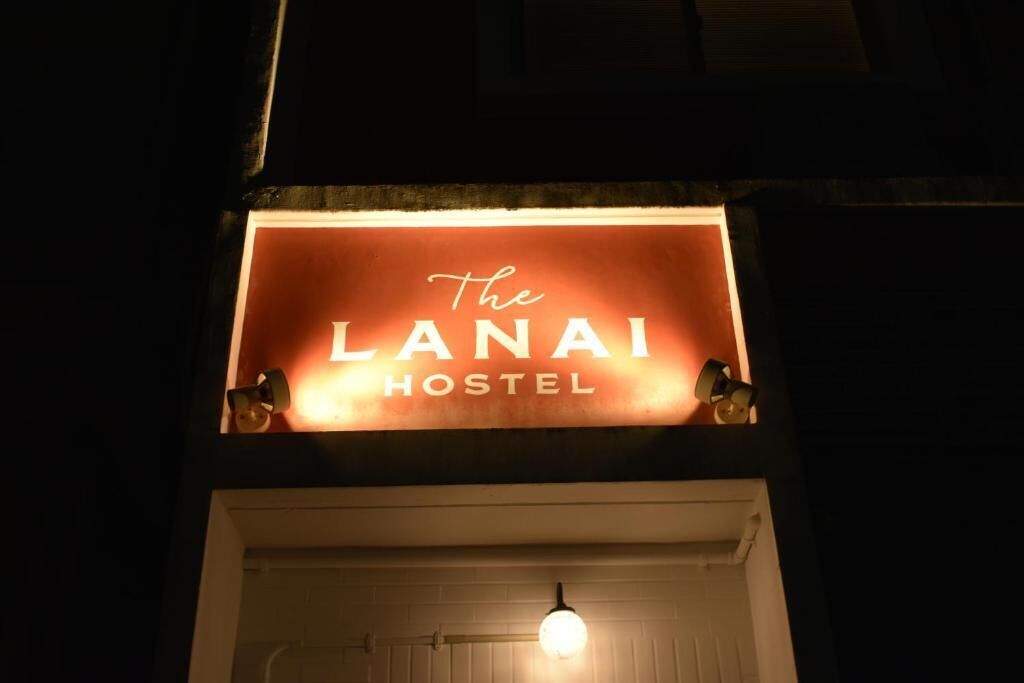 En skylt för ”The Lanai Hostel” med ett varmt ljus och två små dekorativa element på vardera sidan.