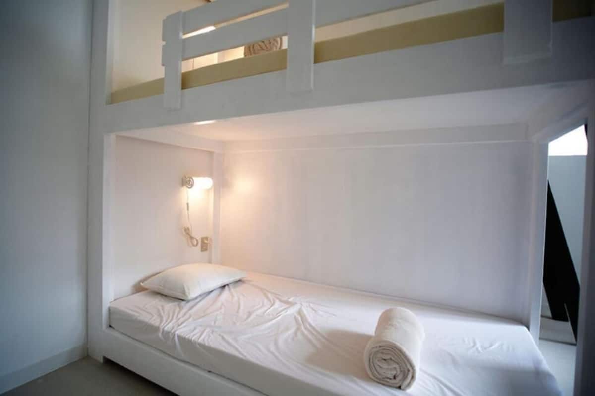 A bunk bed room with a single bed, a wall-mounted light, and a towel on the bed.