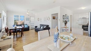 A spacious living area with a dining table, sofa, and kitchen. - Belle Escapes - Life is a Beach (Holdfast Bay)