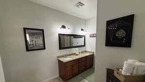 A bathroom with a sink, mirror, framed picture, and a wall-mounted light fixture.