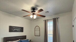 A bedroom with a bed, a ceiling fan, a window with curtains, and a wall with a motivational quote.