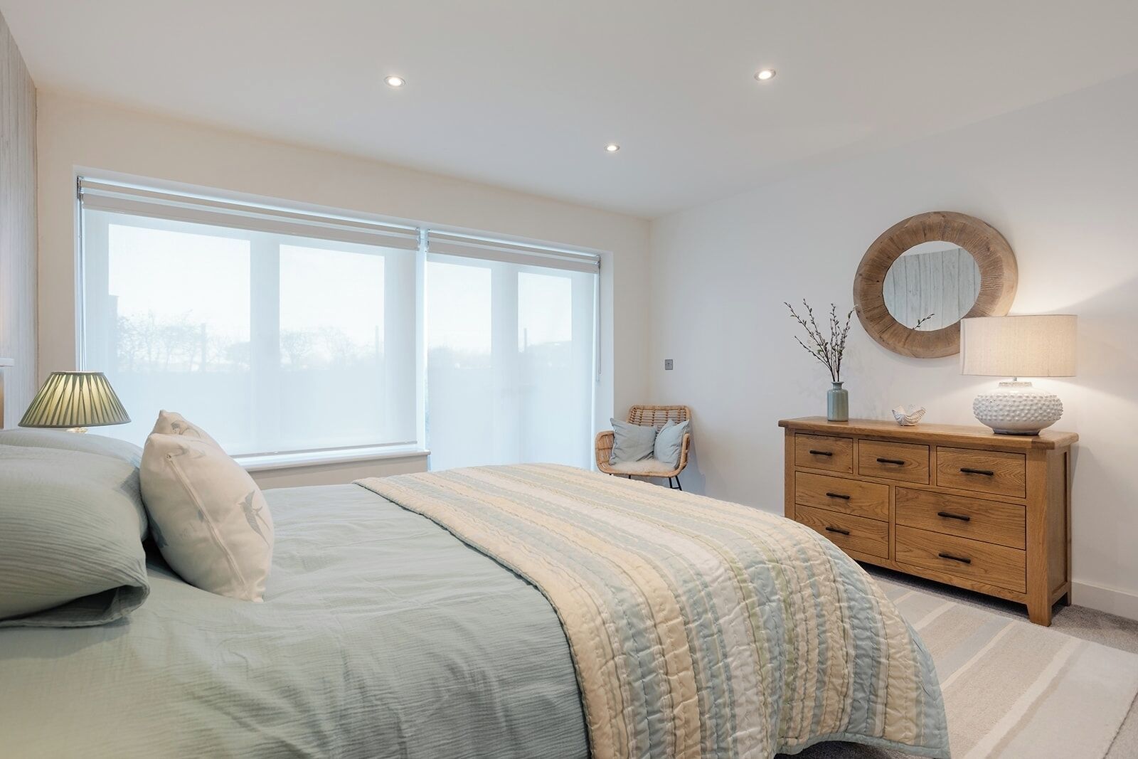 A bedroom with a large bed, a wooden dresser, a chair, and a window with a view.