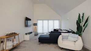 Een moderne woonkamer met een bank, een fauteuil, een televisie en een grote plant.