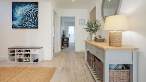 Een gang met een houten vloer, een witte console tafel met schoenen, een lamp en een groot schilderij.
