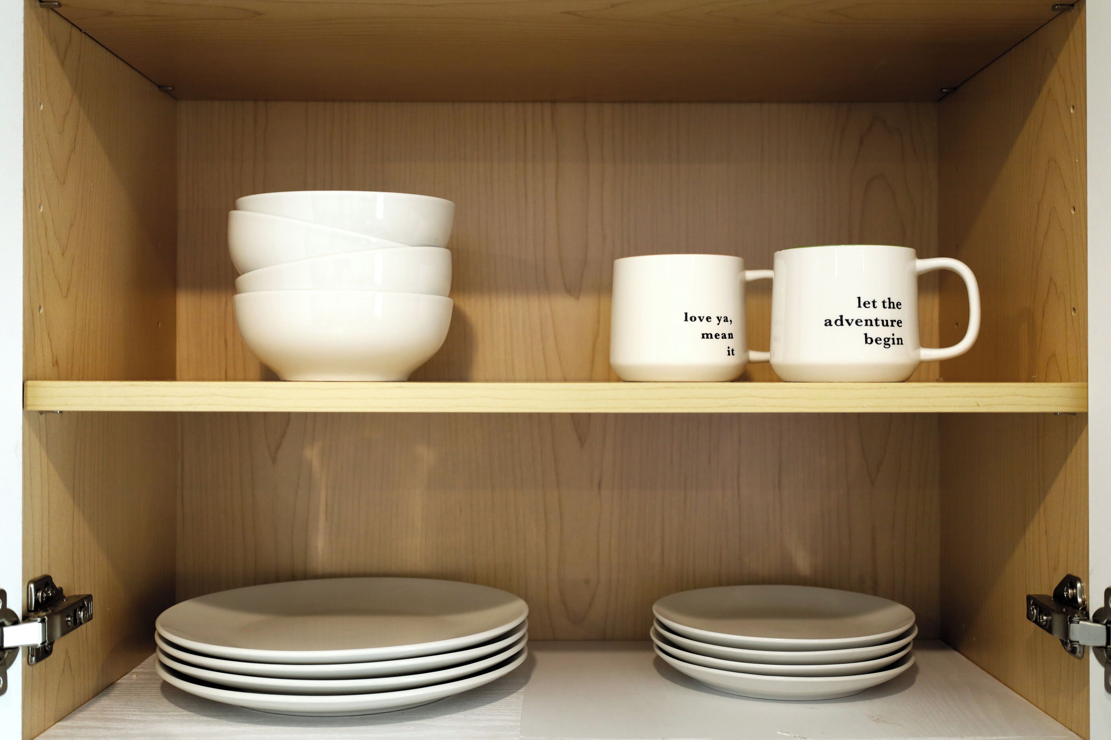 A wooden cabinet with white bowls and mugs on shelves, and stacked plates below.