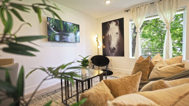 A living room with a sofa, a glass coffee table, a black chair, a painting of a horse, and a window with curtains. - Cozy Downtown Dallas Urban Glow Retreat (Dallas)
