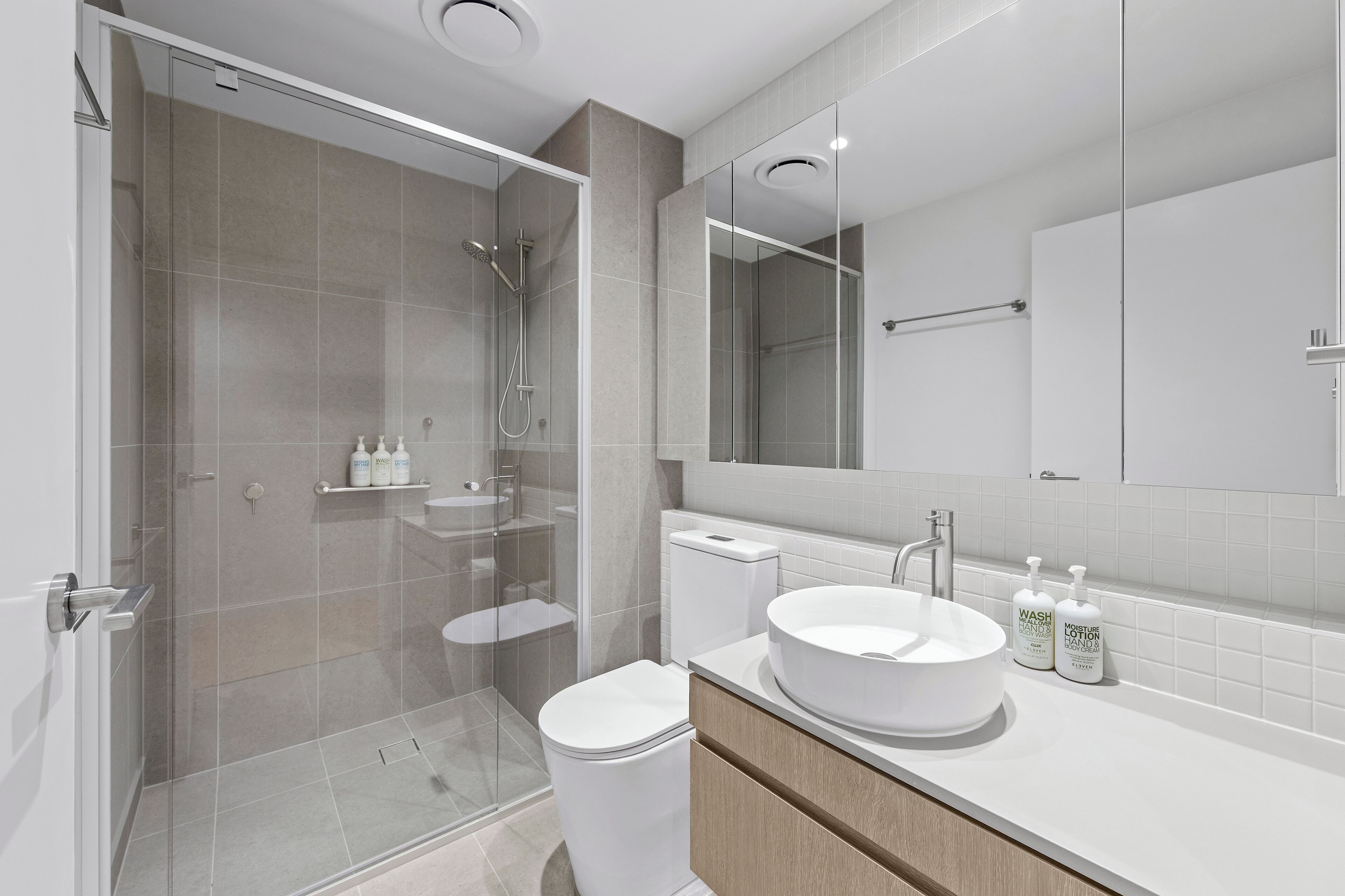 Une salle de bain moderne avec une douche à parois de verre, des toilettes, un lavabo avec un miroir et des articles de toilette posés sur le comptoir.