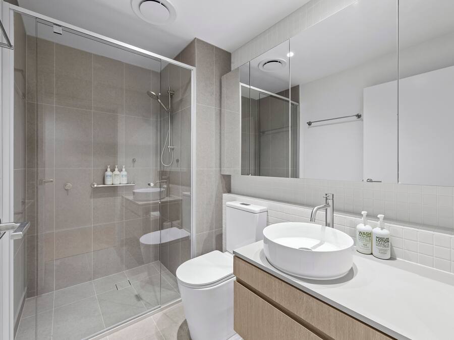 Une salle de bain moderne avec une douche à parois de verre, des toilettes, un lavabo avec un miroir et des articles de toilette posés sur le comptoir.