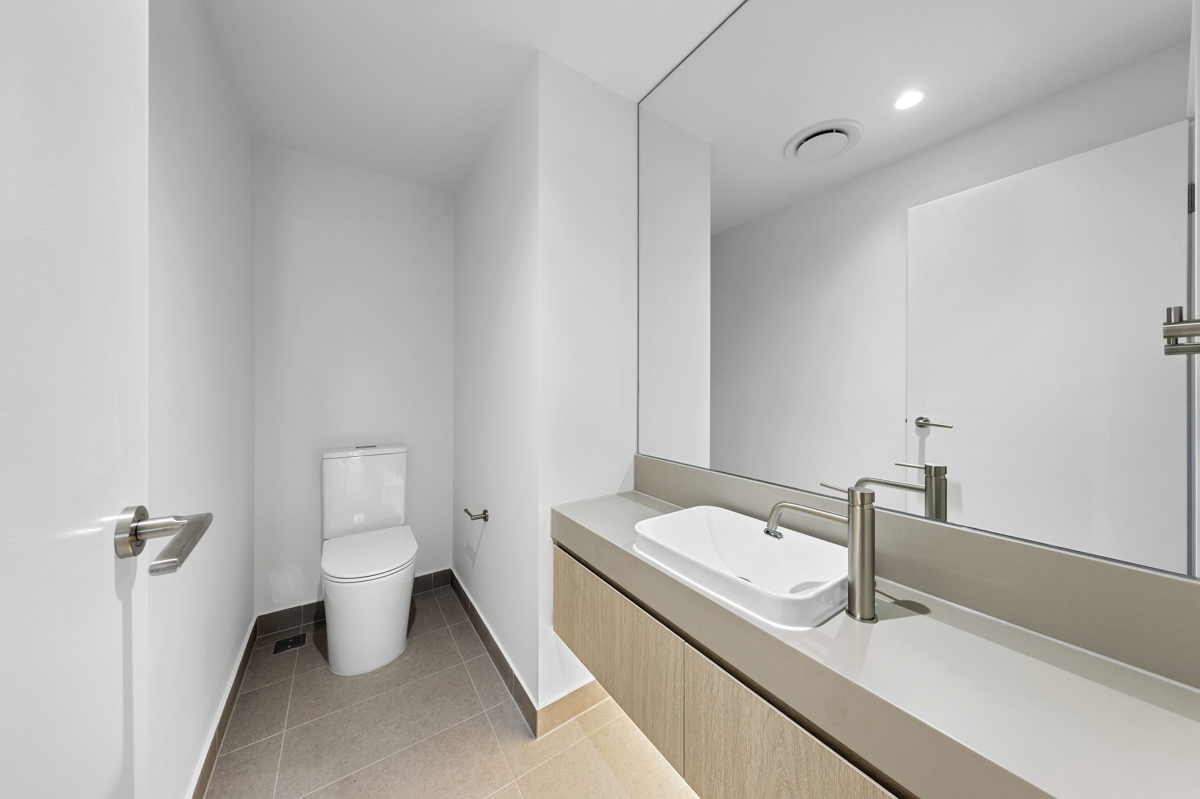 Ein modernes Badezimmer mit Toilette, Waschbecken mit Spiegel und einer Deckenleuchte.
