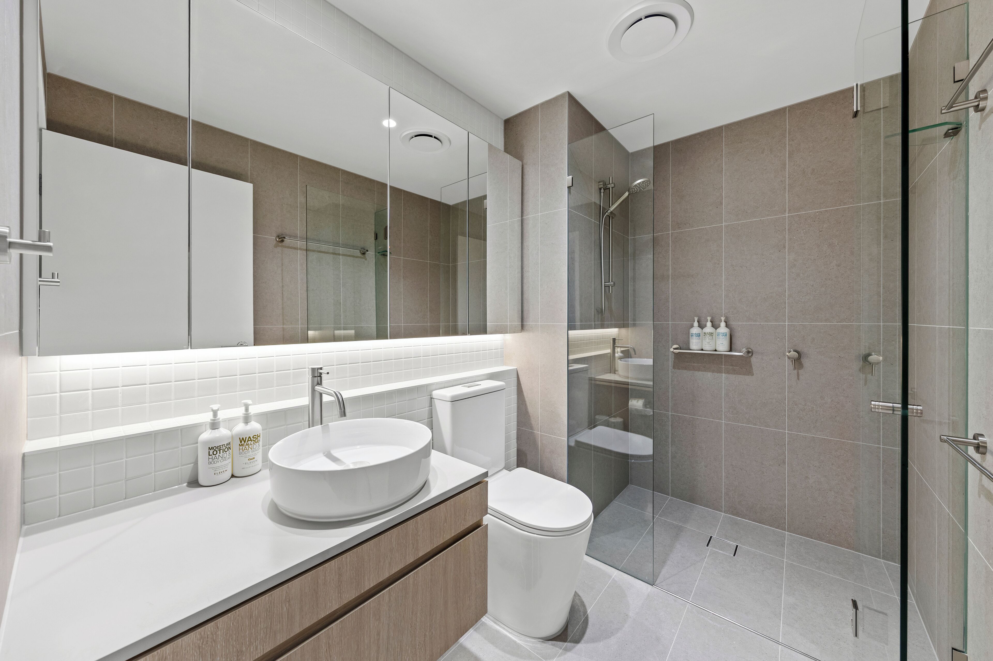 Un baño moderno con un espejo grande, un lavabo redondo, un inodoro y una zona de ducha con mampara de vidrio.