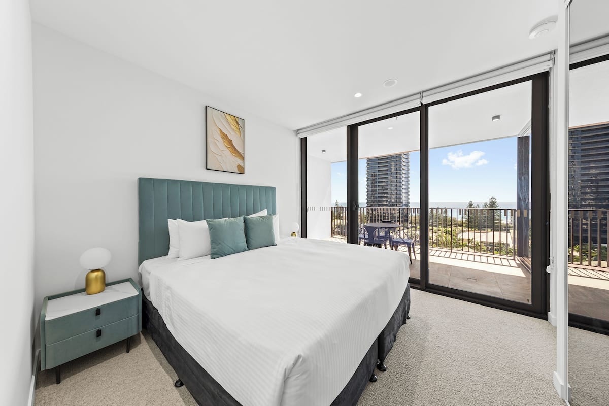 Un dormitorio con una cama grande, una mesita de noche y vistas a un balcón con mobiliario exterior.