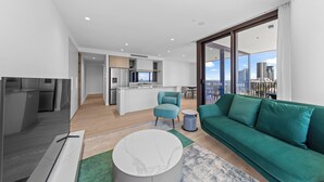 A modern living room with a green sofa, a marble coffee table, and a kitchen in the background. - Yves Mermaid Beach Apartments by CLLIX (Mermaid Beach)