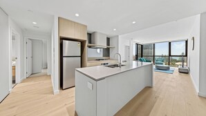 A modern kitchen with a central island, stainless steel appliances, and large windows offering a view of the city. - Yves Mermaid Beach Apartments by CLLIX (Mermaid Beach)