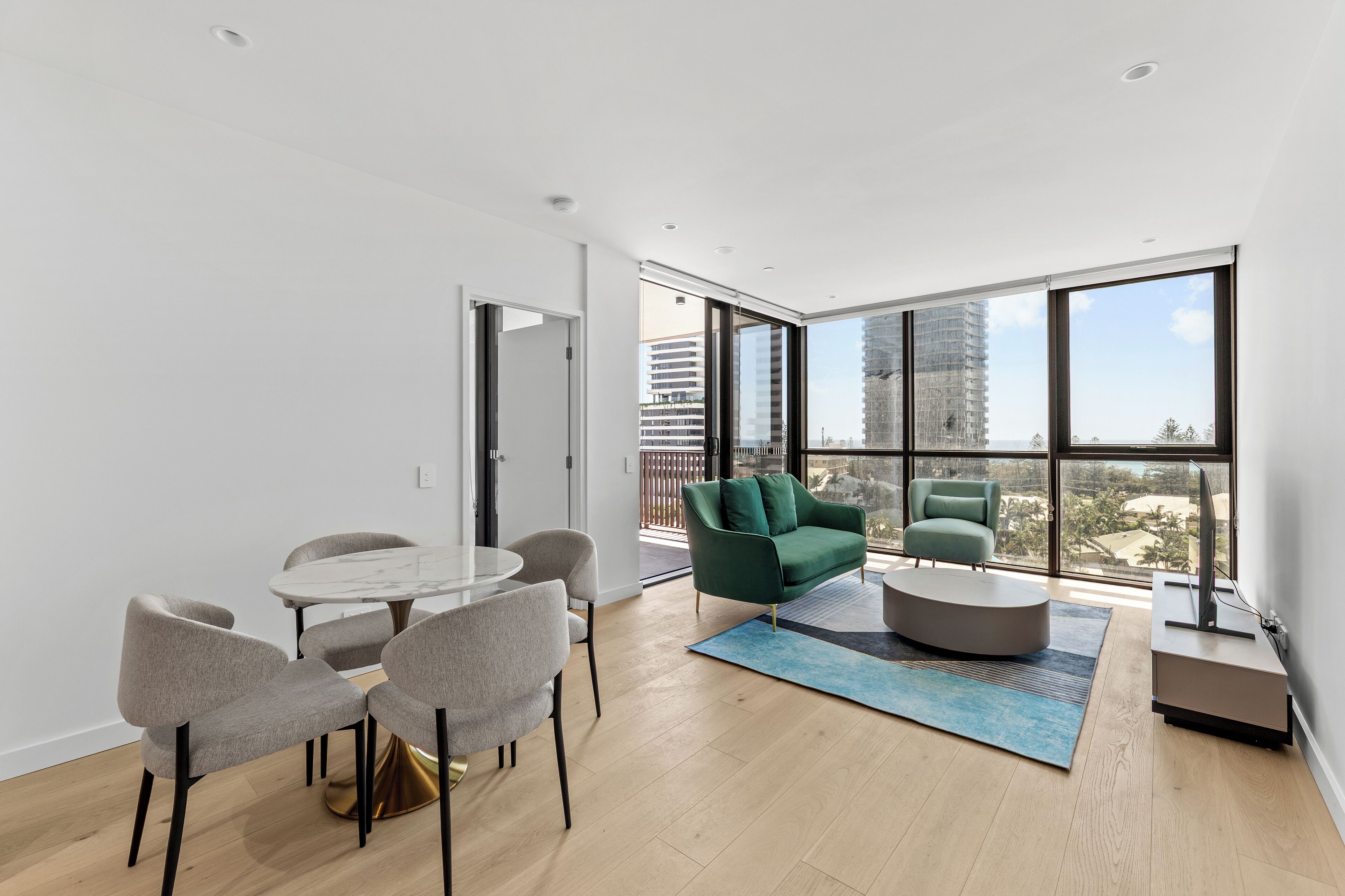 Una sala de estar moderna con comedor, ventanas amplias y vistas a un paisaje urbano.