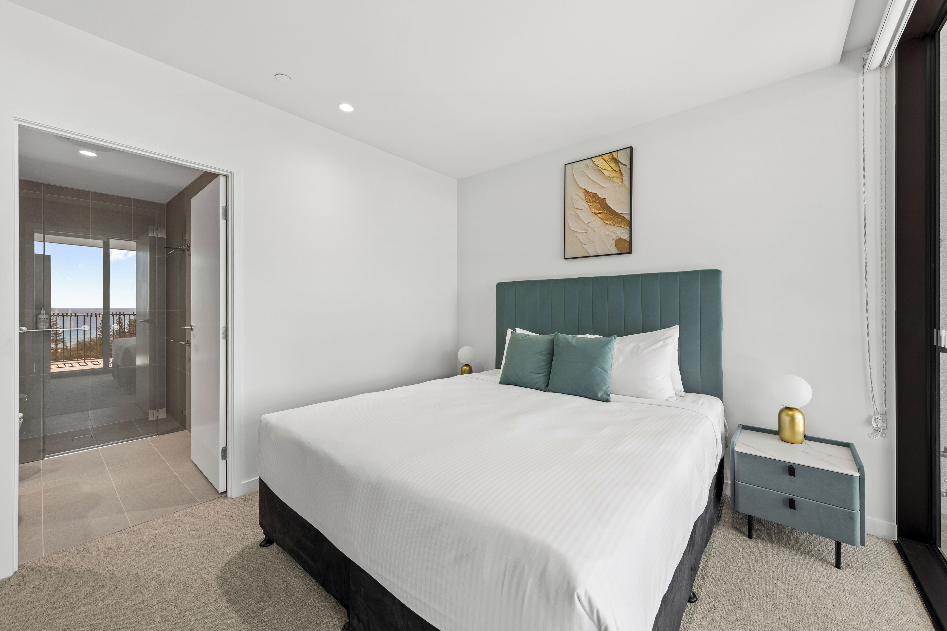 A modern bedroom with a large bed, a nightstand, a wall-mounted lamp, and a glass door leading to a balcony.