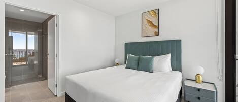 A modern bedroom with a large bed, a nightstand, a wall-mounted lamp, and a glass door leading to a balcony.