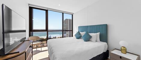 A modern bedroom with a large bed, a TV, and a view of the ocean.