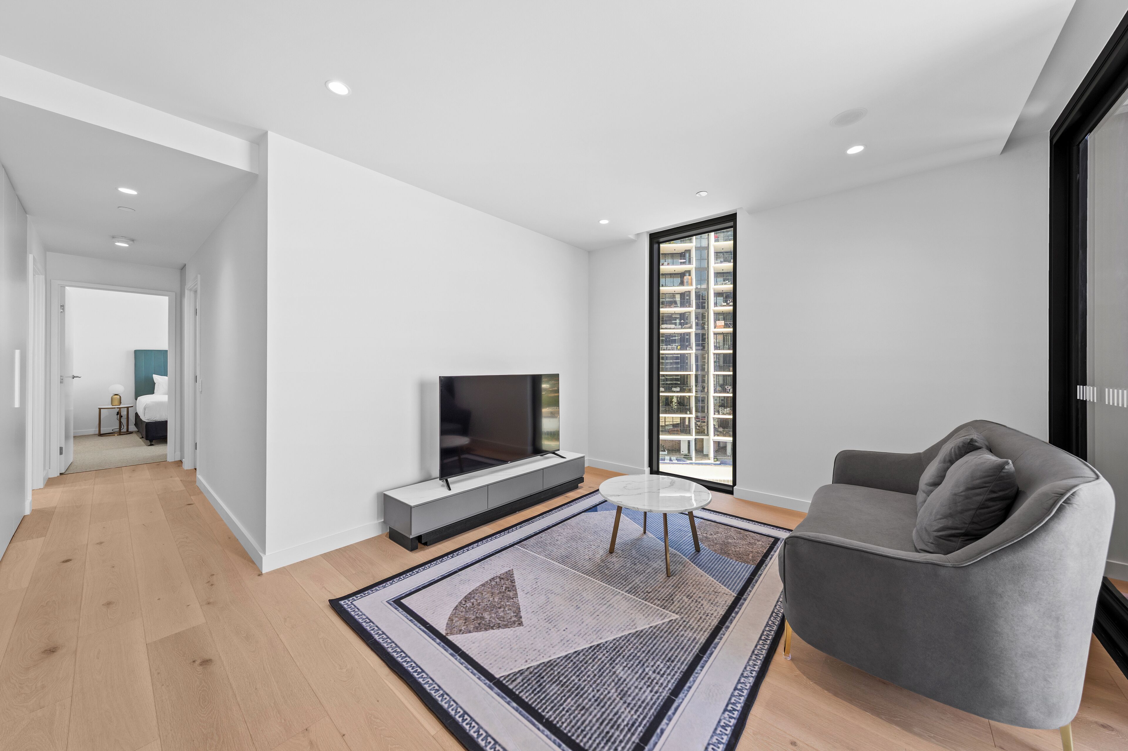 A modern living room with a flat-screen TV, a gray sofa, and a patterned rug.