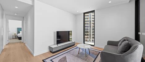 A modern living room with a flat-screen TV, a gray sofa, and a patterned rug.