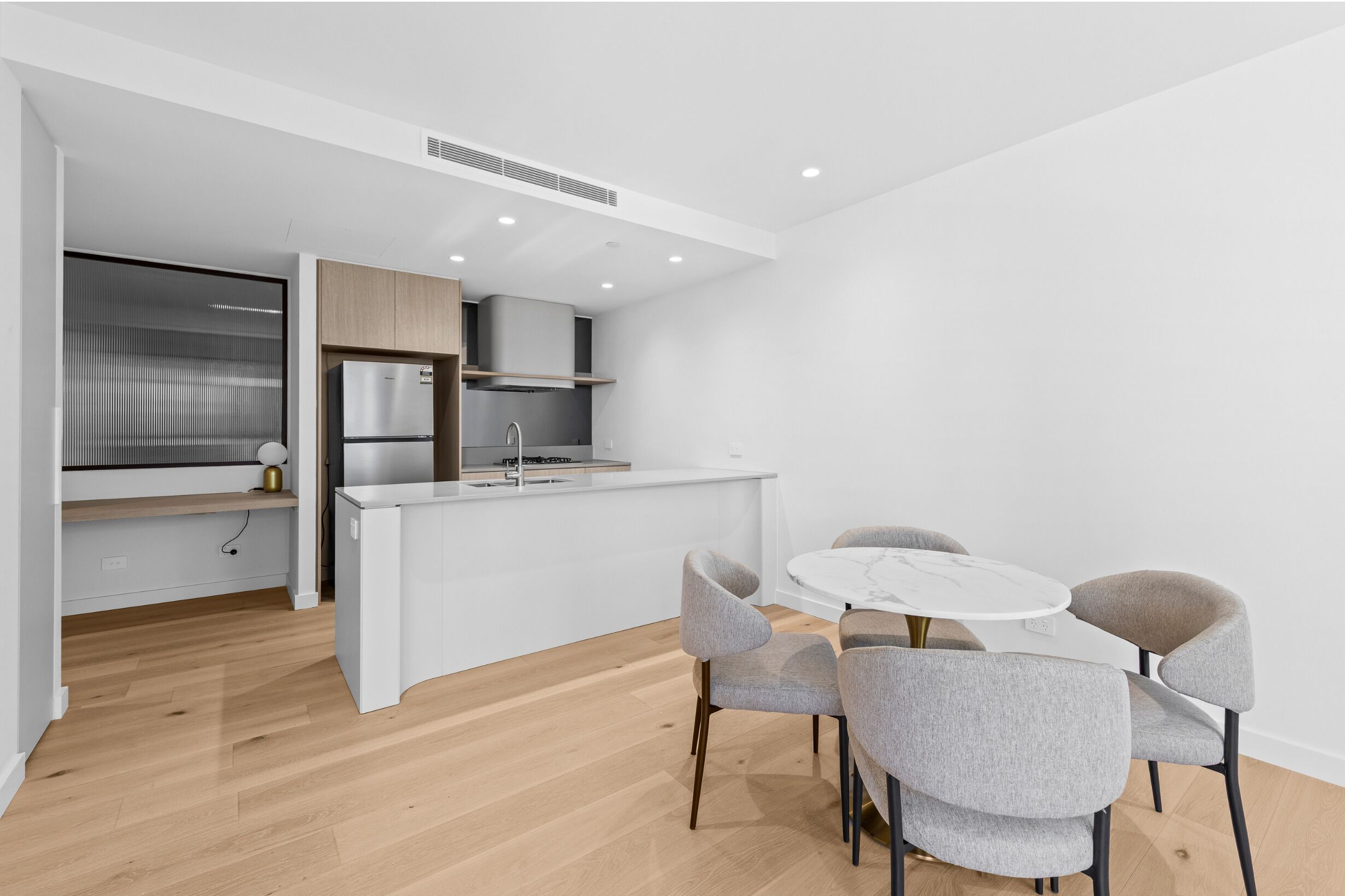 A modern kitchen with a central island, a dining area with four chairs, and a built-in bench with a lamp.