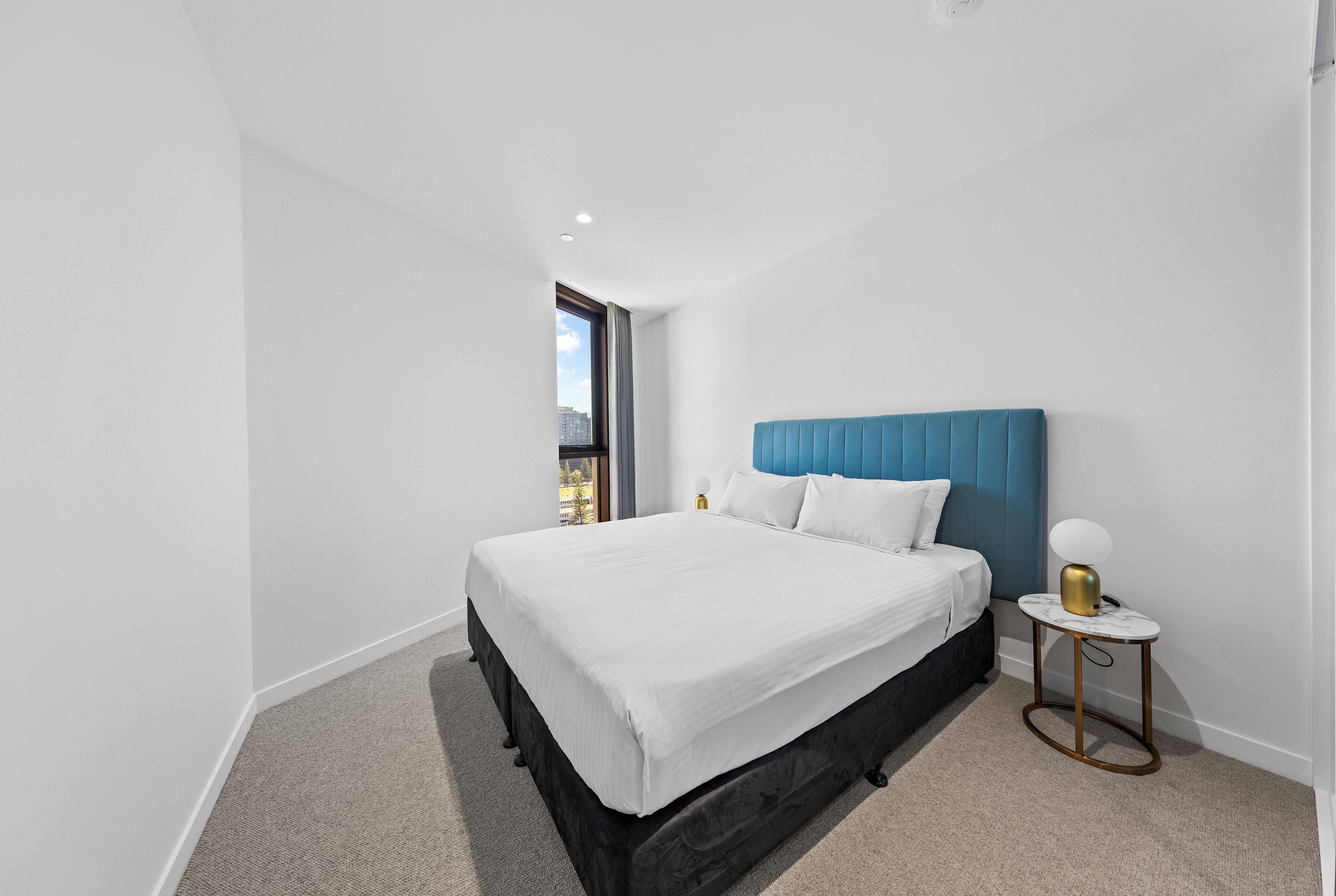 A modern bedroom with a large bed, a blue headboard, and a small bedside table with a lamp.