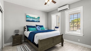 A bedroom with a bed, a nightstand, a ceiling fan, a window with blinds, and an air conditioning unit.