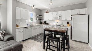 A modern kitchen with white cabinets, a dining table with two chairs, a refrigerator, and a microwave.