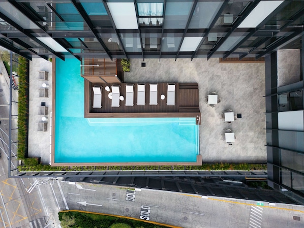 A rooftop pool with lounge chairs and a small seating area, surrounded by modern buildings.