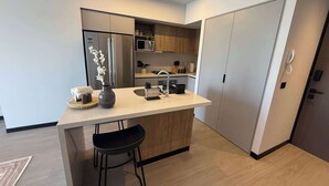 A modern kitchen with a central island, black bar stools, a refrigerator, microwave, and wooden cabinets. - High-floor apartment with city views (Guadalajara)