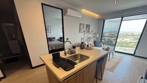 A modern kitchen with a large island, a built-in sink, and a view of the city through large windows. - High-floor apartment with city views (Guadalajara)