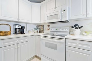 A kitchen with white cabinets, a microwave, a coffee maker, and a stove. - Sunset Bay I 202 (Ocean City)
