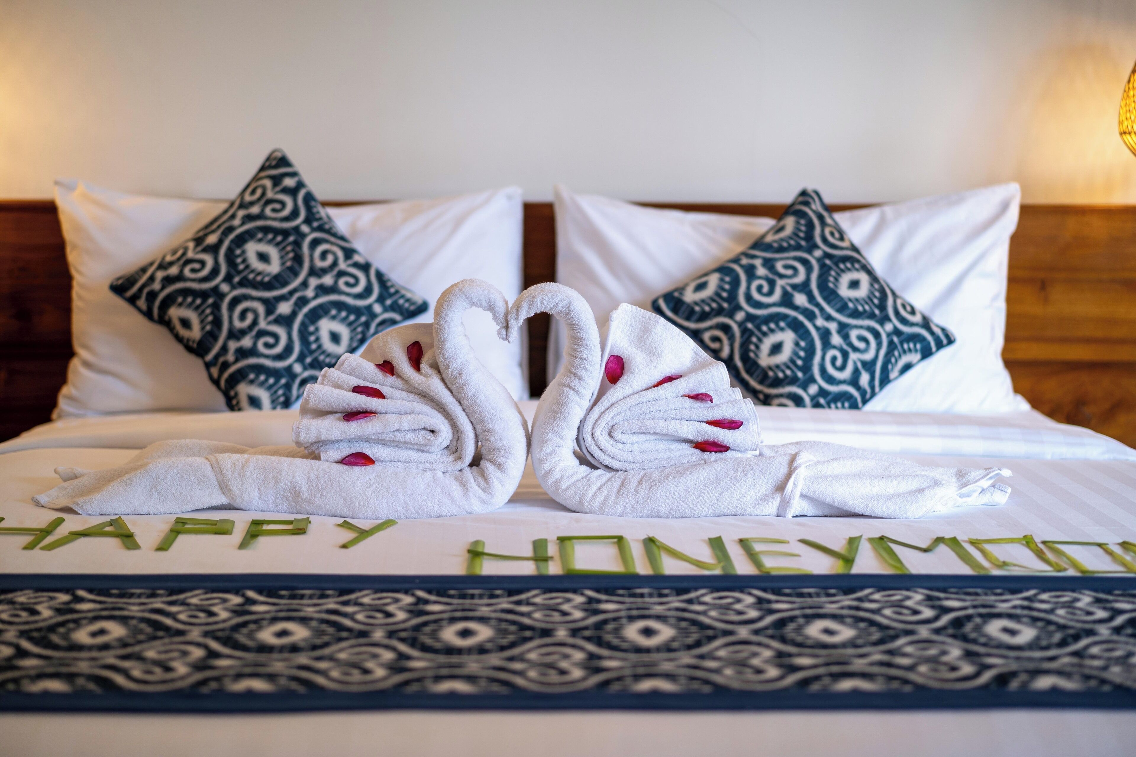 Un lit soigneusement fait, agrémenté d’un message « Joyeuse lune de miel », de coussins à motifs et d’une disposition décorative de serviettes.