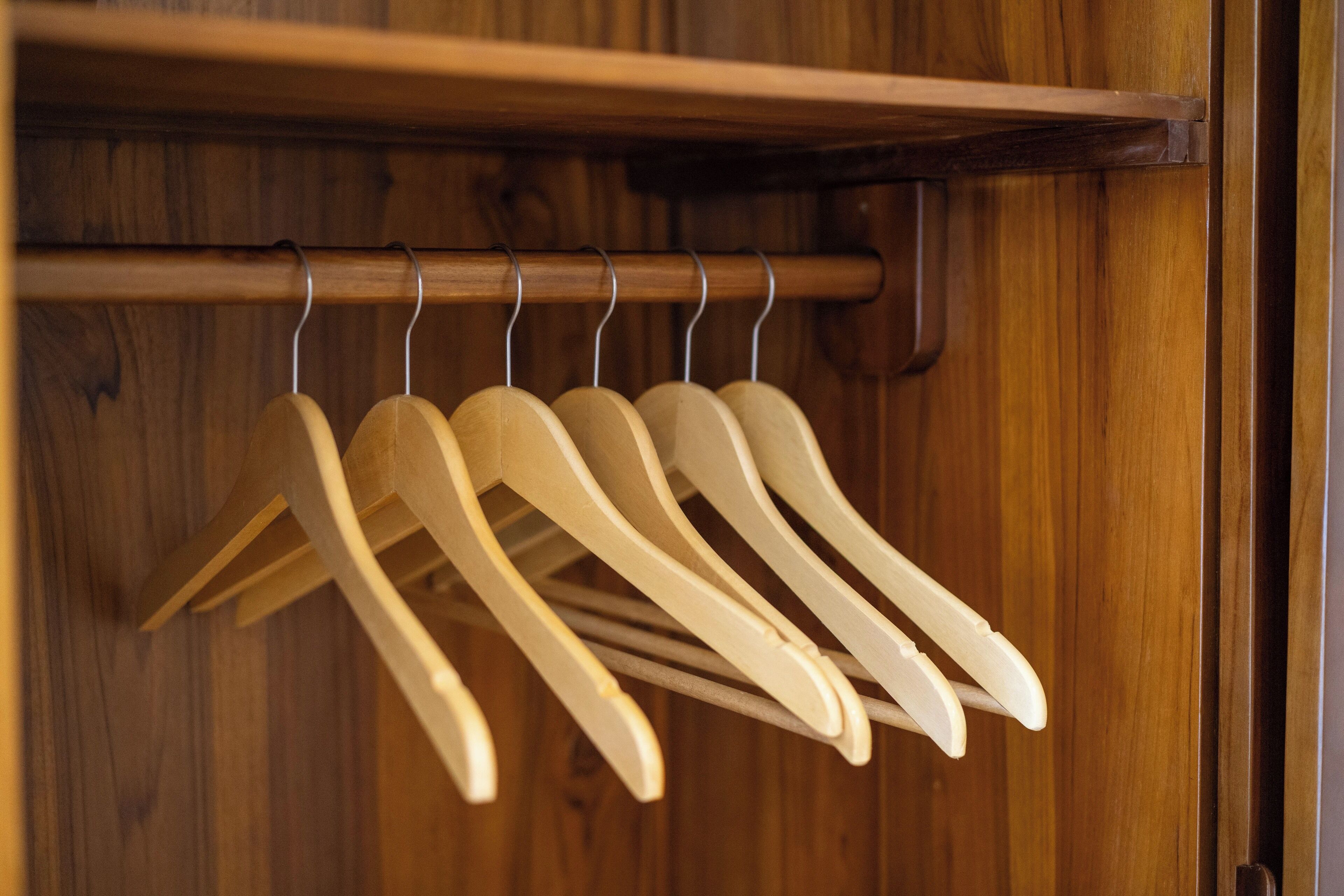 Wooden hangers hanging on a rod in a wooden closet.