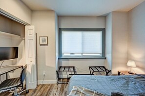 Ein Schlafzimmer mit Bett, Schreibtisch, Stuhl, Fernseher und Fenster.
