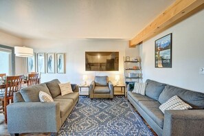 A living room with two sofas, a dining table, and chairs. There is a large window, a wall-mounted TV, and a poster on the wall. - Downtown 2BD 1BA - 2 Blocks to Main/River #187 (Buena Vista)