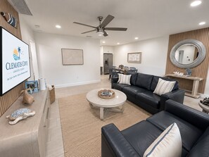 A modern living room with a black leather sofa, a round coffee table, and a ceiling fan. - Clematis Cove • Private Hot Tub + Fenced Yard • Near Downtown & Siesta Key (Sarasota)