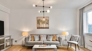 A modern living room with a grey sofa, two side tables with lamps, a coffee table, and a TV on a stand. - Mayfair 2-bed With Private Parking Near Buckingham Palace Green Park (London)