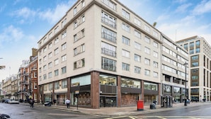 A multi-story building with a modern facade, large windows, and a ground-level entrance with a glass storefront. - Mayfair 2-bed With Private Parking Near Buckingham Palace Green Park (London)
