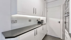 A modern kitchen with white cabinetry, a black countertop, and a kettle. - Mayfair 2-bed With Private Parking Near Buckingham Palace Green Park (London)