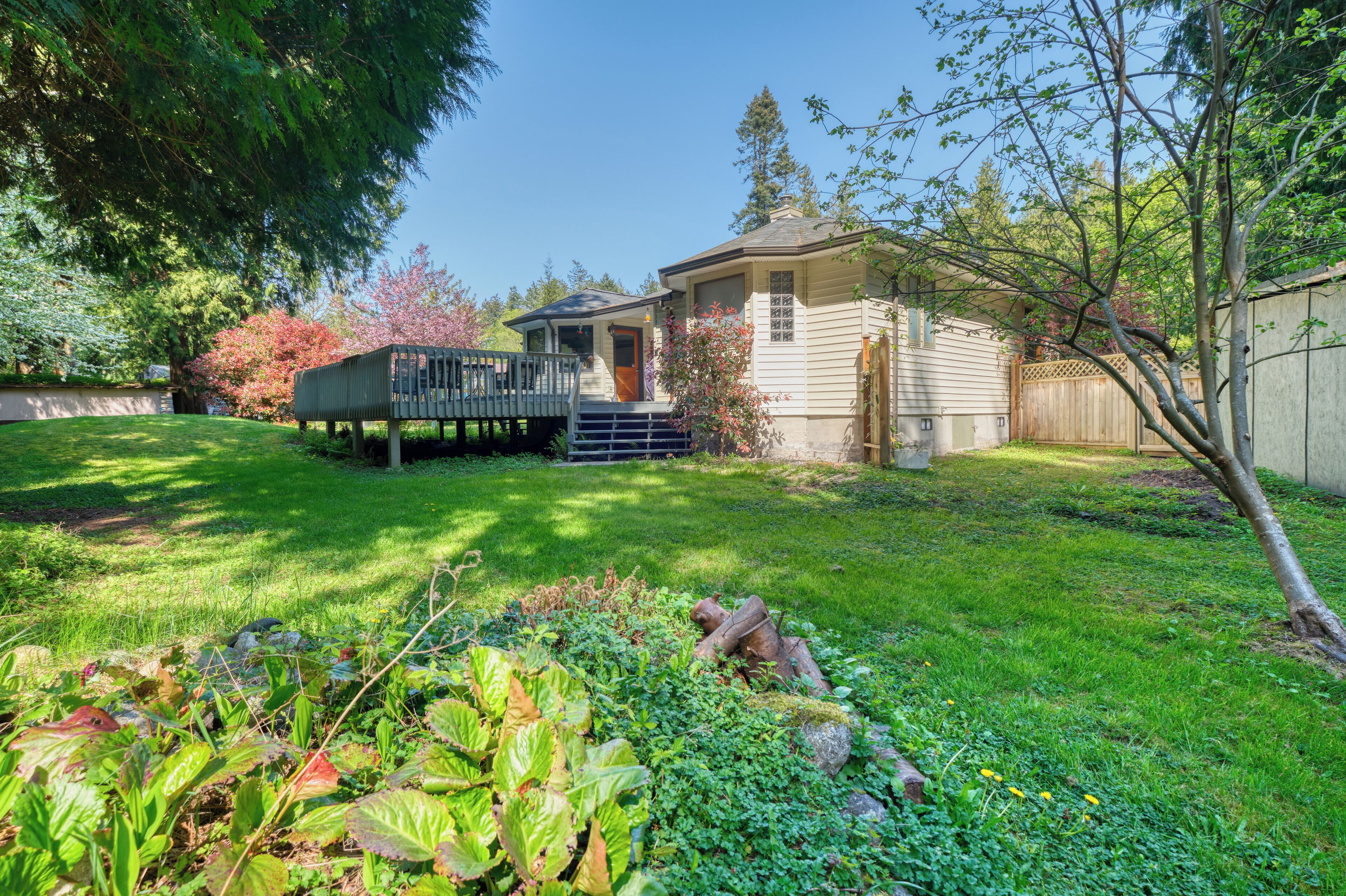 A house with a deck, surrounded by a well-maintained garden and trees.