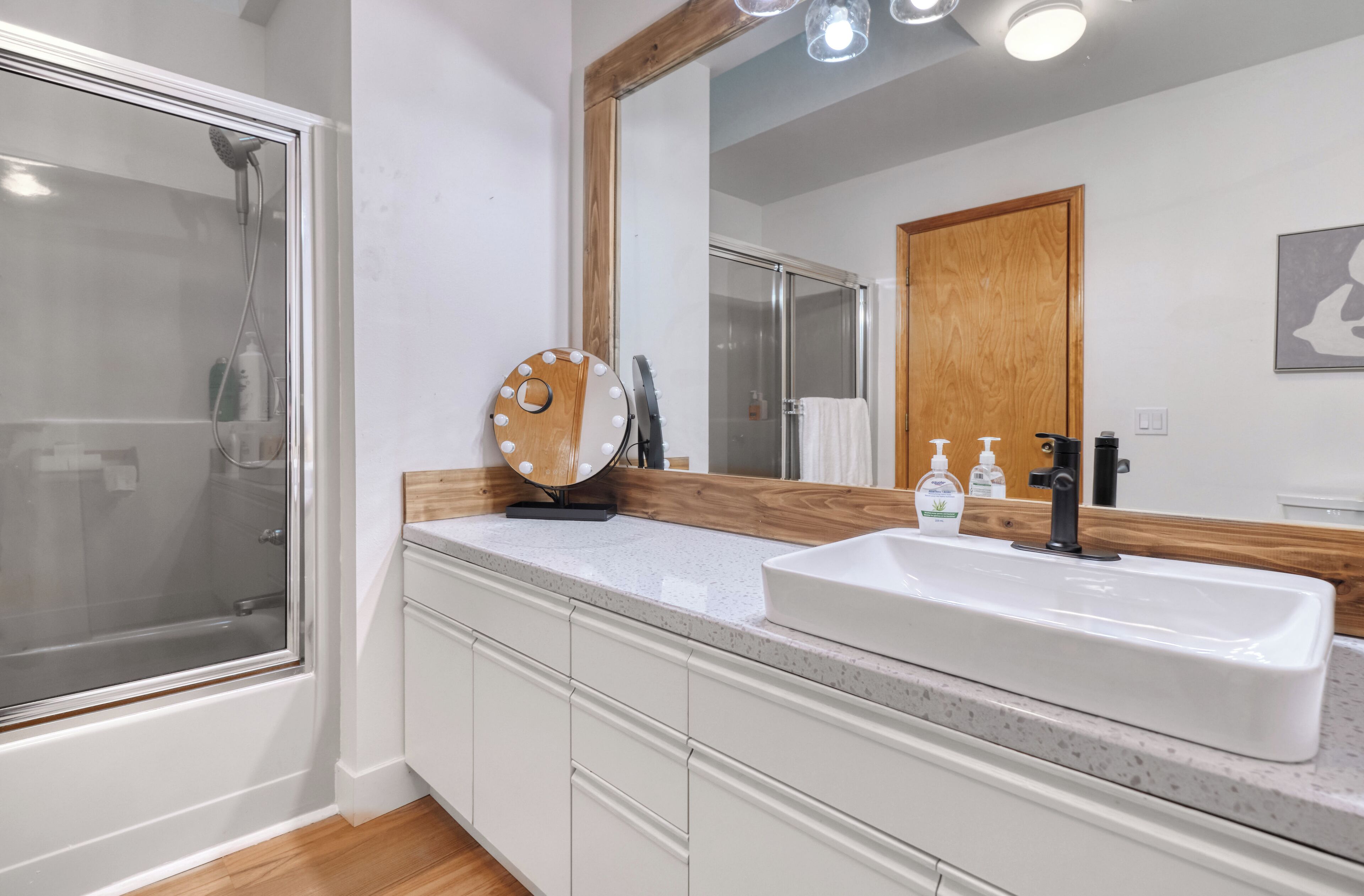 A modern bathroom with a large mirror, a white sink, and a shower enclosure.