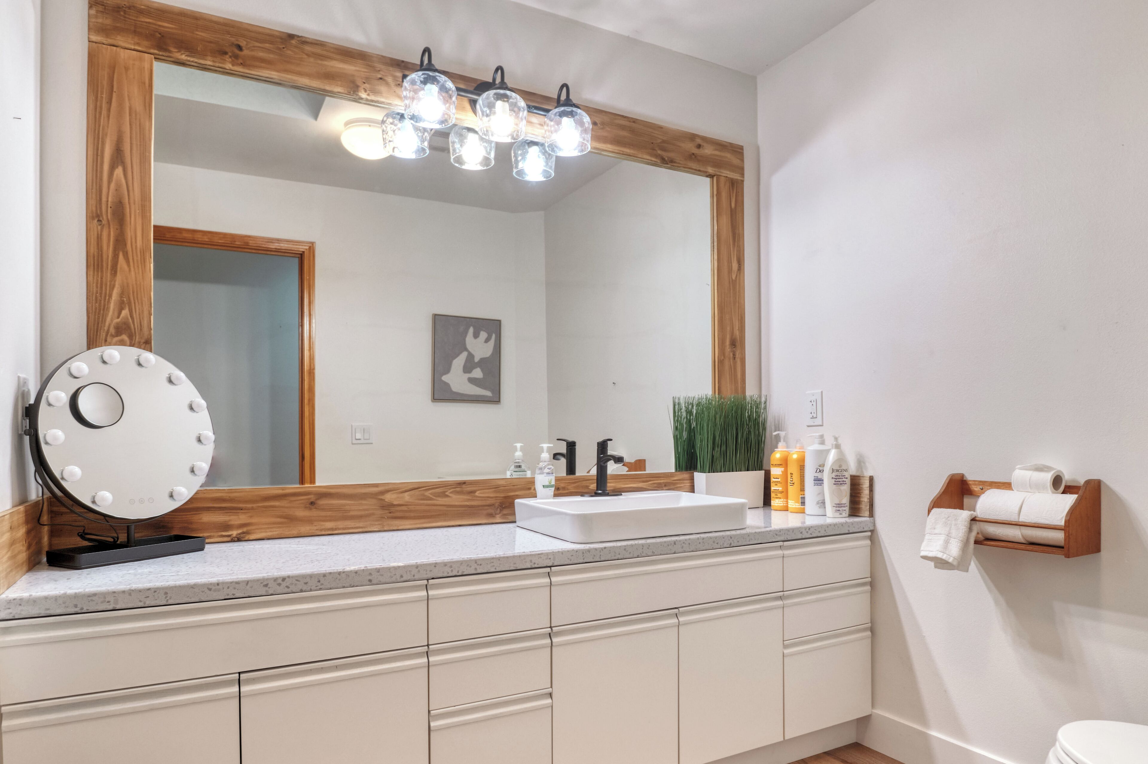 A bathroom with a large mirror, vanity, and a wooden-framed light fixture.