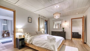 Une chambre avec un lit en bois, des lampes de chevet, un miroir et une vue sur le salon.