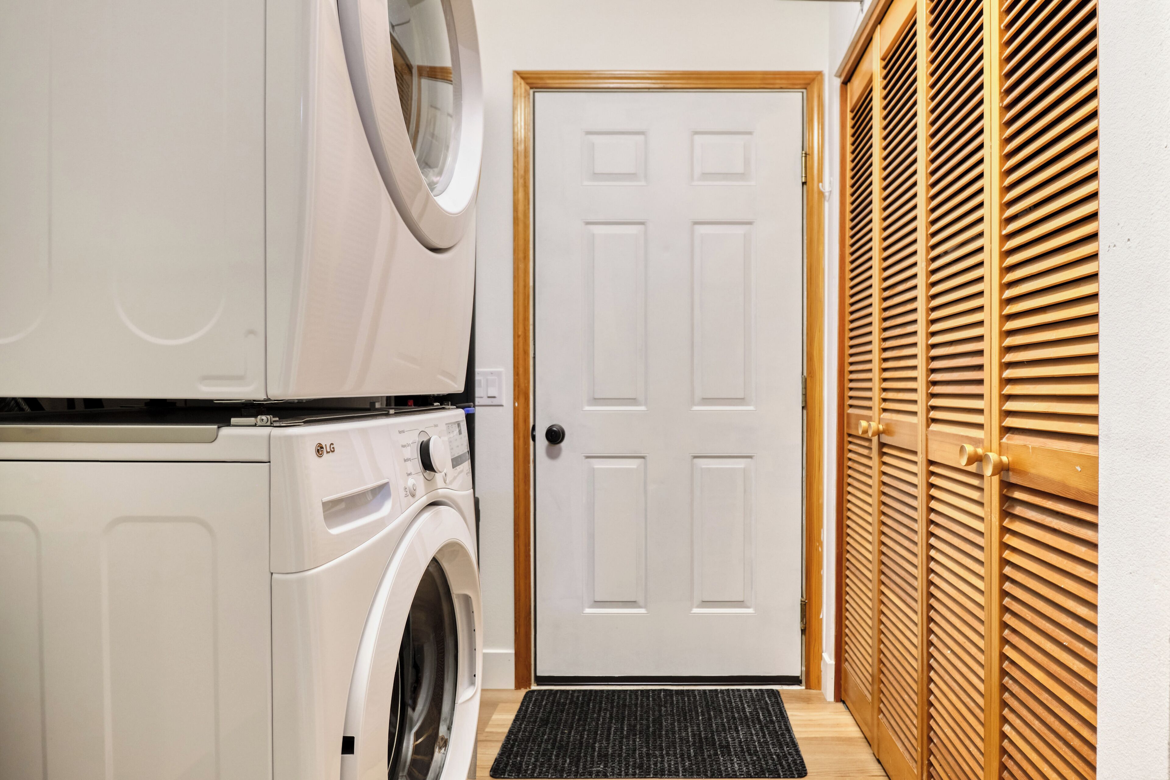 A laundry room with a front-loading washer and dryer, a white door, and wooden louvered closets.